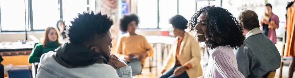 Students smiling and talking in a classroom with other students studying in background